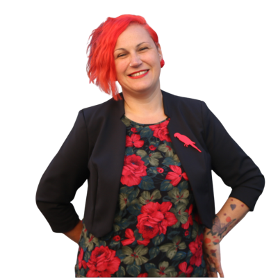 An image of Natalie Walker, a woman with bright red hair wearing a bold dress with a rise print and a black jacket over the top.