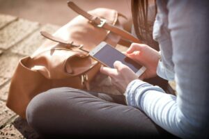 a person sitting cross-legged holding a phone and texting. There is a tan leather bag in front of them